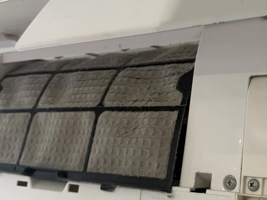 Filtres de climatisation recouverts d'une couche de poussière grise et feutrée, avant rinçage